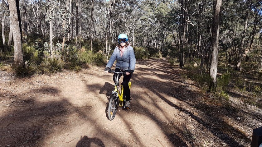 Castlemaine to Maldon Trail - Fe cycling through a lightly wooded forest towards the camera
